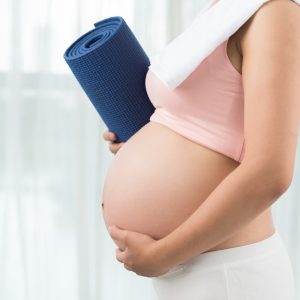Cropped image of sporty pregnant woman with yoga mat